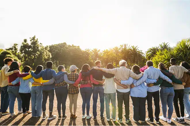A group of people standing in a line turned away from the camera, with arms wrapped around each other.