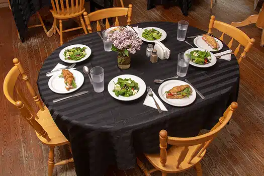 A 4-place table setting with black tablecloth, and healthy salads and sandwiches on plates accompanied with glasses of water.